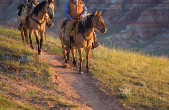 A man and a woman on horses look into the sunset near CM Ranch in Dubois, WY | Wyoming dude ranch