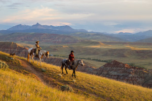 A man and a woman ride a trail above a rocky ridgeline at sunset near CM Ranch in Dubois, WY | Wyoming dude ranch