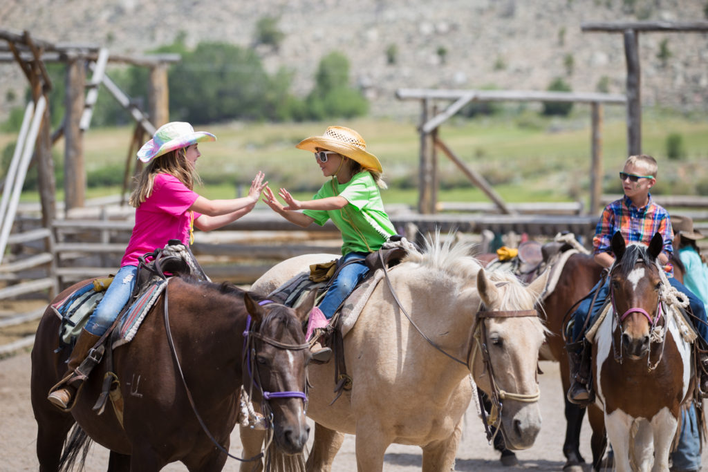 Two girls share a double high-five on horseback at CM Ranch in Dubois, WY | Dude Ranch Wyoming Family