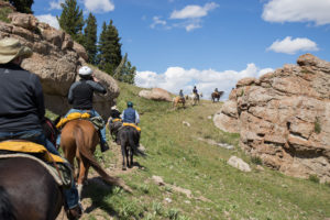 Riders on horseback ride a trail through rocky outcroppings near CM Ranch in Dubois, WY