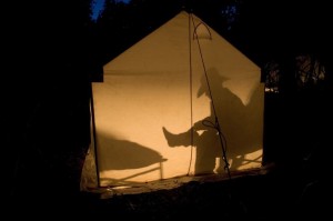 A man is seen in silhouette removing his boot inside his tent lit from within on a horseback riding wyoming trip at CM Ranch