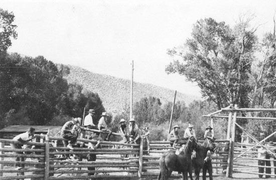 Ranch hands sit on a lodgepole fence near horses at historic CM Ranch in Dubois, WY | Wyoming guest ranches