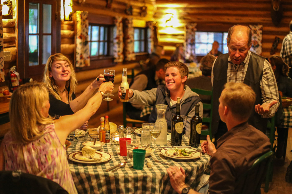 A small group of people at a dinner table raise a toast wyoming dude ranches for families