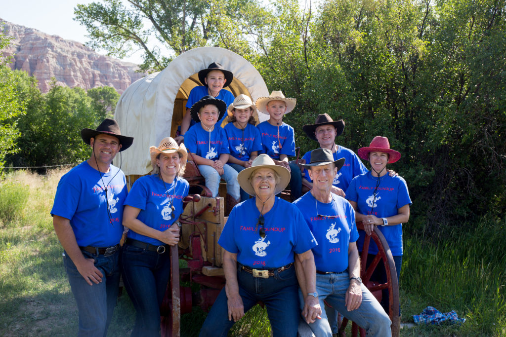 A family wearing matching blue t-shirts poses for a photo on a covered wagon at CM Ranch in Dubois, WY | affordable family dude ranch vacations