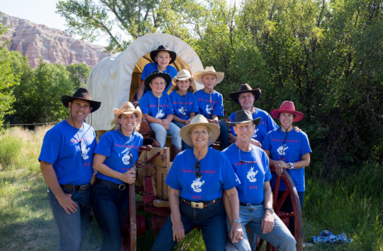A family wearing matching blue t-shirts poses for a photo on a covered wagon at CM Ranch in Dubois, WY | affordable family dude ranch vacations